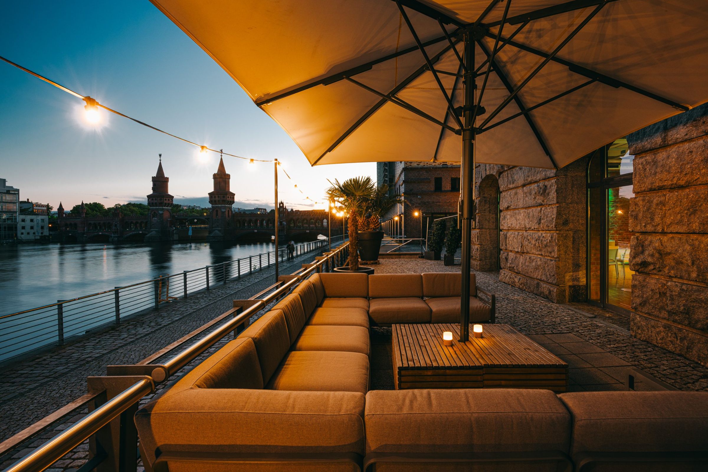 Spreeterrasse mit Lounge-Möbeln und Blick auf die Oberbaumbrücke am Abend